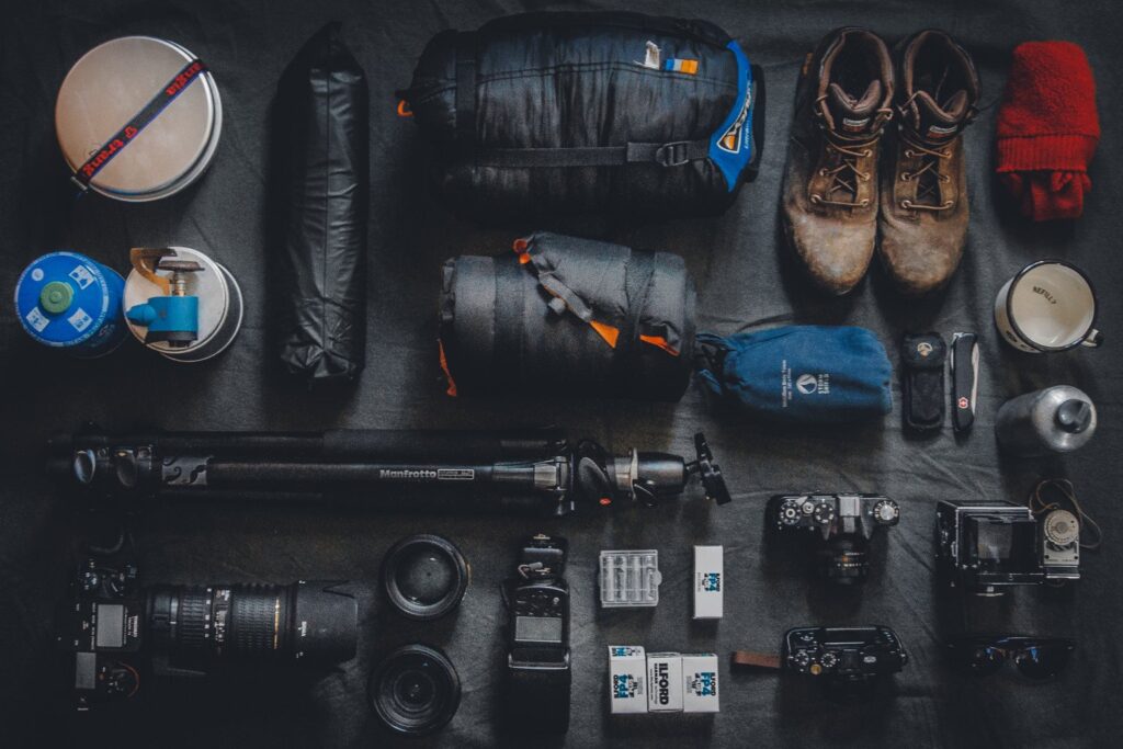 Fotoausrüstung mit Kameras, Objektiven, Stativ und Wanderausrüstung auf dunklem Untergrund