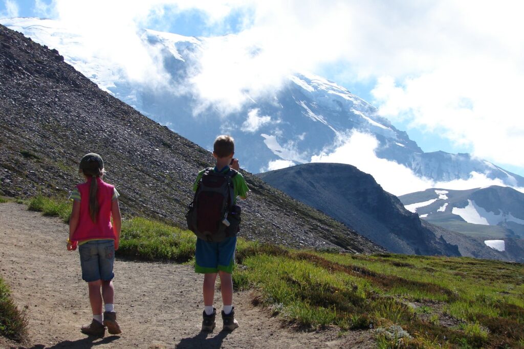 Zwei Kinder mit Rucksäcken auf einem Wanderweg in den Bergen