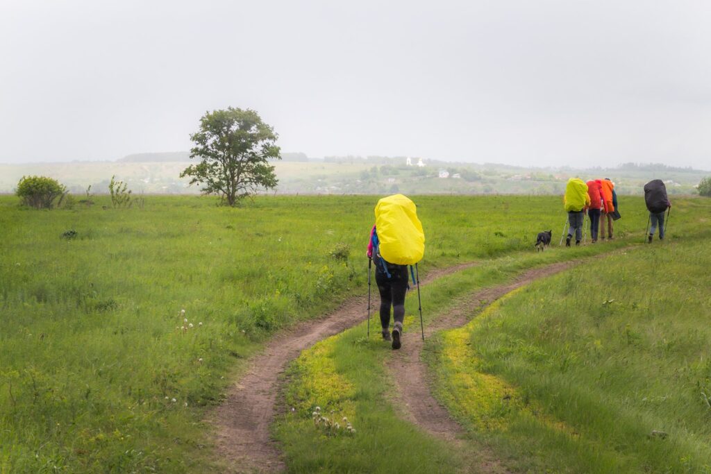 Wanderer mit gelber Regenhülle über dem Rucksack auf einem Feldweg
